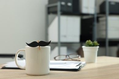 Photo of Happy Father's Day. Cup with paper moustache and clipboard on wooden table, closeup