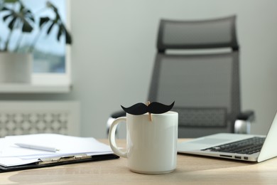 Photo of Happy Father's Day. Cup with paper moustache, clipboard and laptop on wooden table