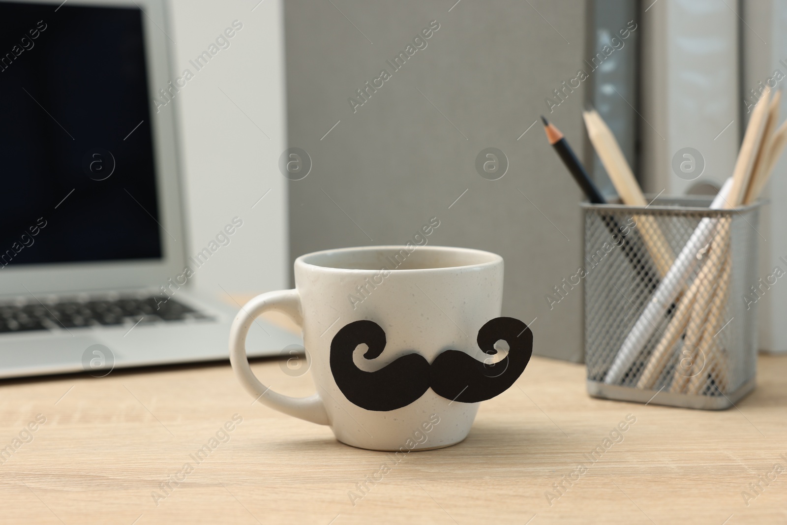 Happy Father's Day. Cup with paper moustache and laptop on wooden table, closeup Photo of Happy Father's Day. Cup with paper moustache and laptop on wooden table, closeup