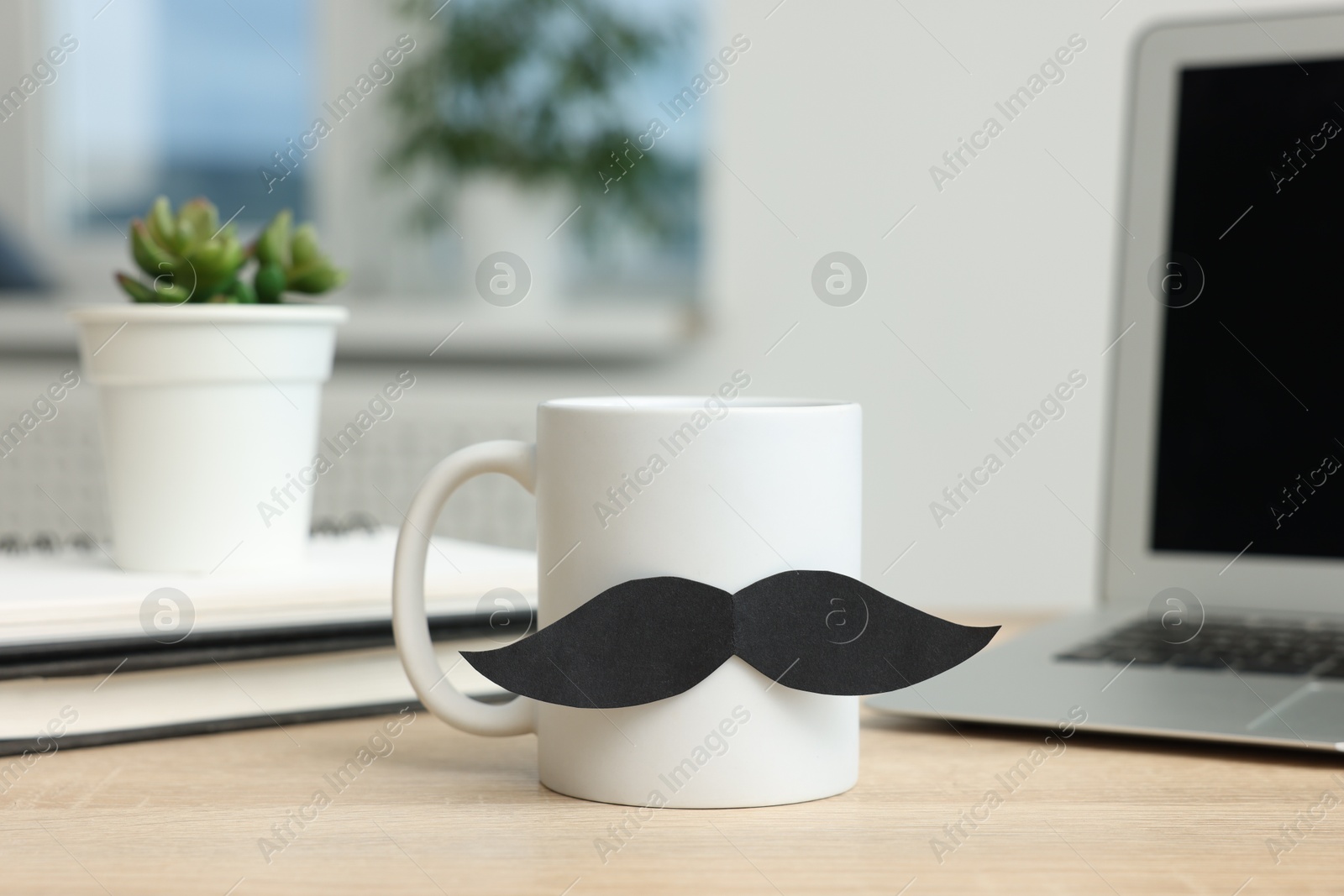 Happy Father's Day. Cup with paper moustache and laptop on wooden table, closeup Photo of Happy Father's Day. Cup with paper moustache and laptop on wooden table, closeup