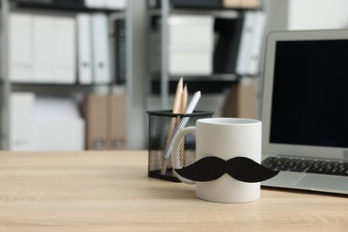 Photo of Happy Father's Day. Cup with paper moustache and laptop on wooden table, space for text