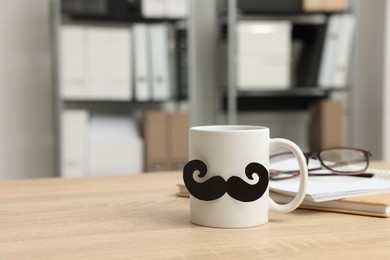 Photo of Happy Father's Day. Cup with paper moustache, books and glasses on wooden table, space for text