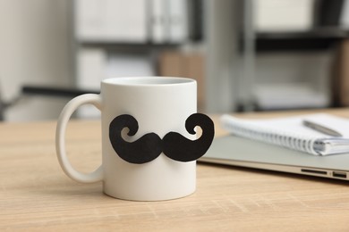 Photo of Happy Father's Day. Cup with paper moustache and books on wooden table, closeup
