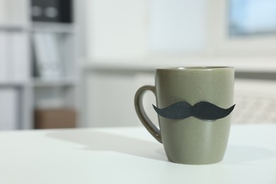 Photo of Happy Father's Day. Cup with paper moustache on white table indoors, closeup. Space for text