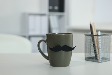Photo of Happy Father's Day. Cup with paper moustache on white table indoors