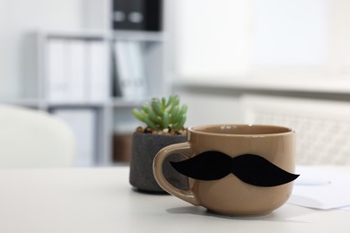 Photo of Happy Father's Day. Cup with paper moustache on white table indoors, closeup