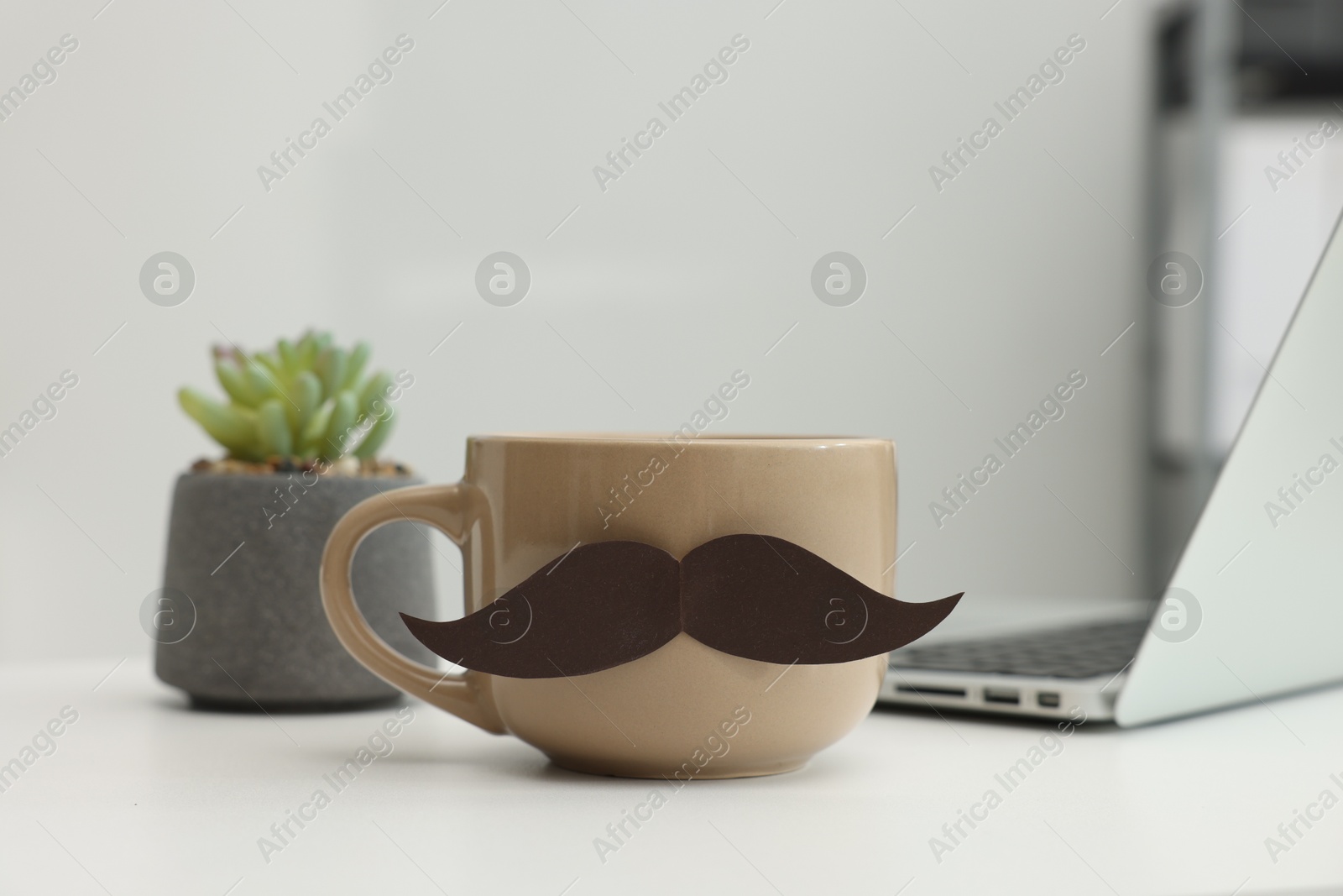 Happy Father's Day. Cup with paper moustache and laptop on white table indoors, closeup Photo of Happy Father's Day. Cup with paper moustache and laptop on white table indoors, closeup