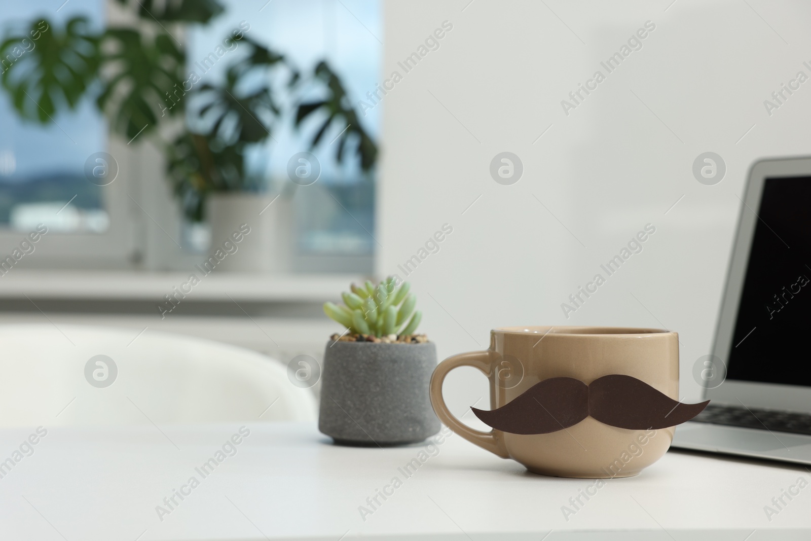 Happy Father's Day. Cup with paper moustache and laptop on white table indoors, space for text Photo of Happy Father's Day. Cup with paper moustache and laptop on white table indoors, space for text
