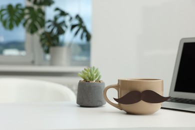 Photo of Happy Father's Day. Cup with paper moustache and laptop on white table indoors, space for text