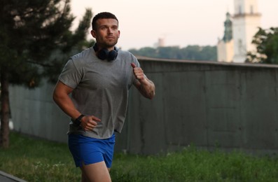 Photo of Athletic young man in sportswear running outdoors, space for text