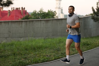 Photo of Athletic young man in sportswear running outdoors, space for text