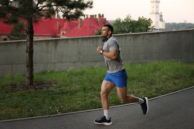 Photo of Athletic young man in sportswear running outdoors, space for text