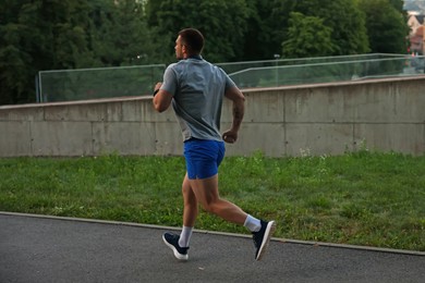 Photo of Athletic young man in sportswear running outdoors, back view