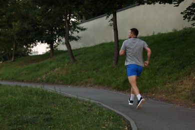 Photo of Athletic young man in sportswear running outdoors, back view. Space for text