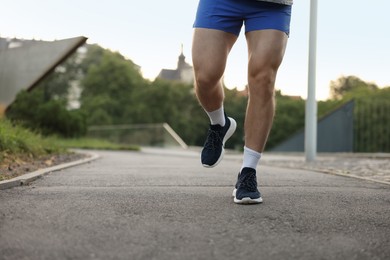 Photo of Athletic young man in sportswear running outdoors, closeup. Space for text