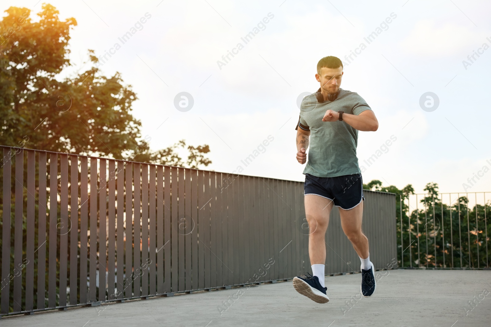Photo of Athletic young man in sportswear running and checking fitness tracker outdoors, space for text