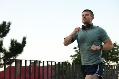 Photo of Athletic young man in sportswear running outdoors, low angle view. Space for text
