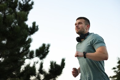 Photo of Athletic young man in sportswear running outdoors, low angle view. Space for text