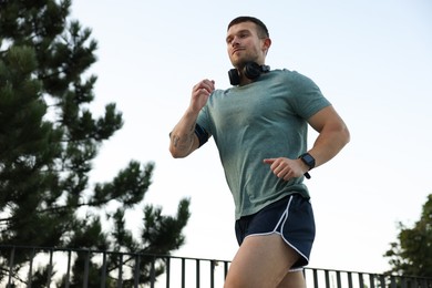 Photo of Athletic young man in sportswear running outdoors, low angle view