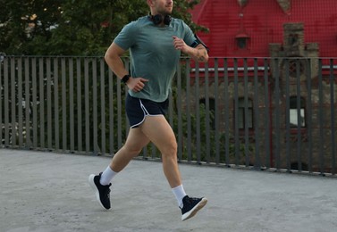 Photo of Athletic young man in sportswear running outdoors, closeup