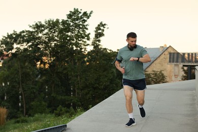 Photo of Athletic young man in sportswear running and checking fitness tracker outdoors, space for text