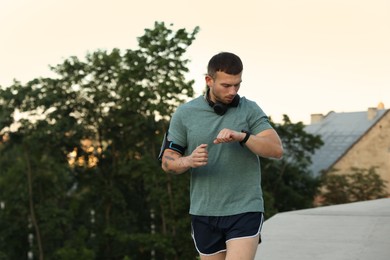 Photo of Athletic young man in sportswear running and checking fitness tracker outdoors