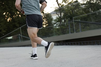 Photo of Athletic young man in sportswear running outdoors, closeup. Space for text