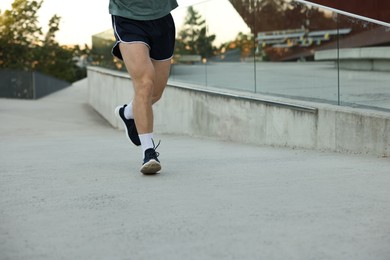 Photo of Athletic young man in sportswear running outdoors, closeup. Space for text