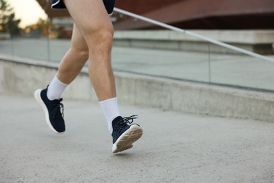 Photo of Athletic young man in sportswear running outdoors, closeup. Space for text