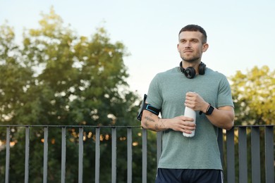 Photo of Athletic young man in sportswear with bottle of water before running outdoors, space for text