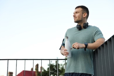 Photo of Athletic young man in sportswear with bottle of water before running outdoors, low angle view. Space for text