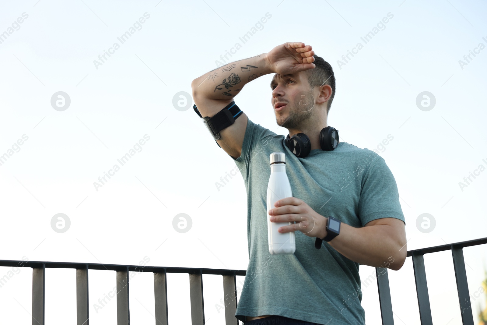 Photo of Athletic young man in sportswear with bottle of water before running outdoors, low angle view