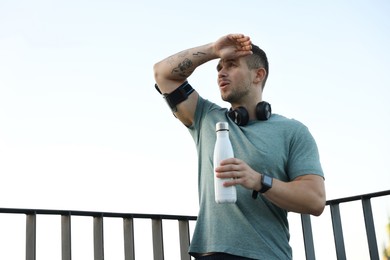 Photo of Athletic young man in sportswear with bottle of water before running outdoors, low angle view