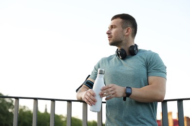 Photo of Athletic young man in sportswear with bottle of water before running outdoors, low angle view. Space for text