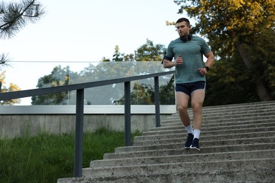 Photo of Athletic young man in sportswear running down stairs outdoors, low angle view. Space for text