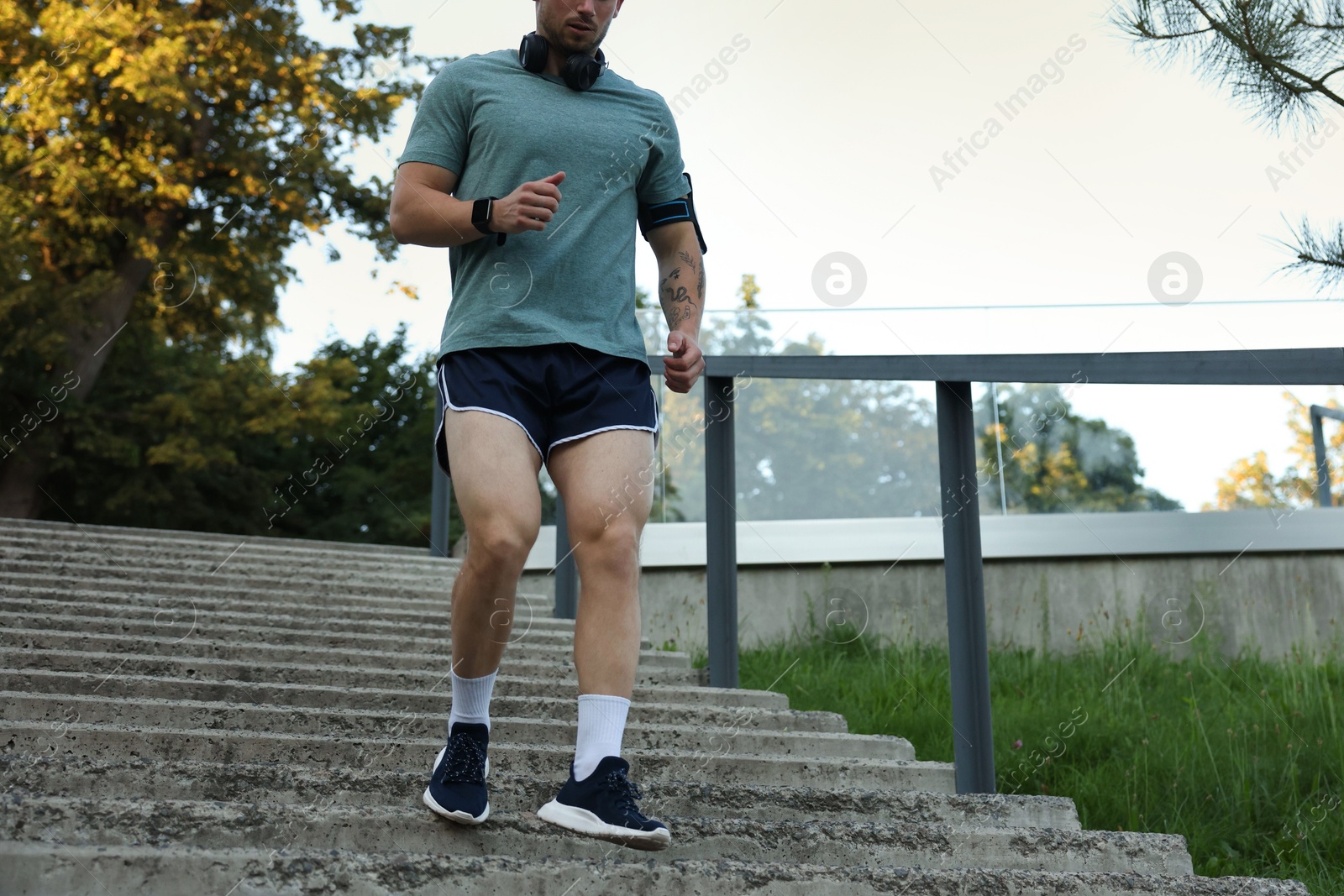 Photo of Athletic young man in sportswear running down stairs outdoors, closeup. Space for text