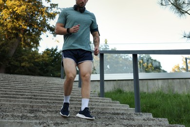 Photo of Athletic young man in sportswear running down stairs outdoors, closeup. Space for text