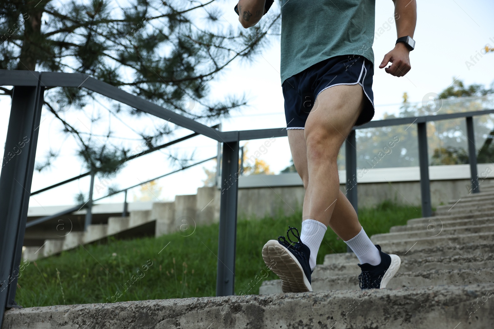 Photo of Athletic young man in sportswear running down stairs outdoors, closeup. Space for text