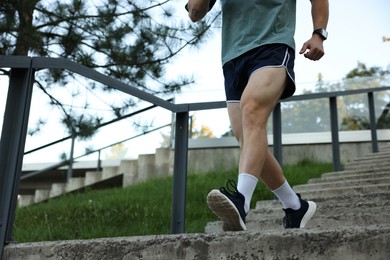 Photo of Athletic young man in sportswear running down stairs outdoors, closeup. Space for text