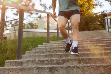 Photo of Athletic young man in sportswear running down stairs outdoors, closeup