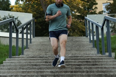 Photo of Athletic young man in sportswear running down stairs outdoors, closeup