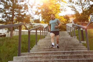 Photo of Athletic young man in sportswear running down stairs outdoors, low angle view