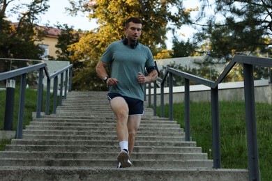Photo of Athletic young man in sportswear running down stairs outdoors, low angle view