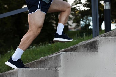 Photo of Athletic young man in sportswear running up stairs outdoors, closeup