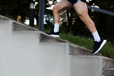 Photo of Athletic young man in sportswear running up stairs outdoors, closeup
