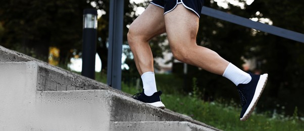 Photo of Athletic young man in sportswear running up stairs outdoors, closeup