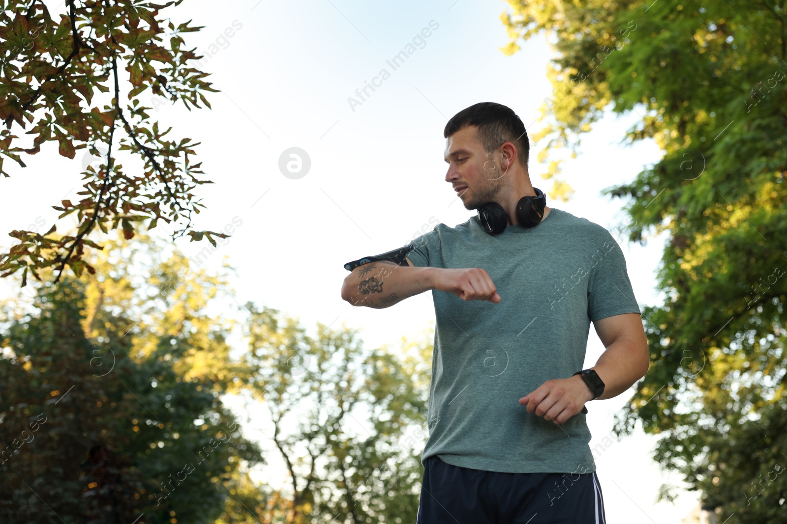 Athletic young man in sportswear checking fitness tracker before running outdoors, low angle view. Space for text Photo of Athletic young man in sportswear checking fitness tracker before running outdoors, low angle view. Space for text