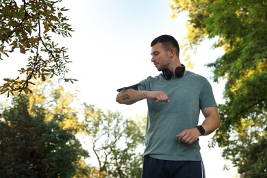 Photo of Athletic young man in sportswear checking fitness tracker before running outdoors, low angle view. Space for text