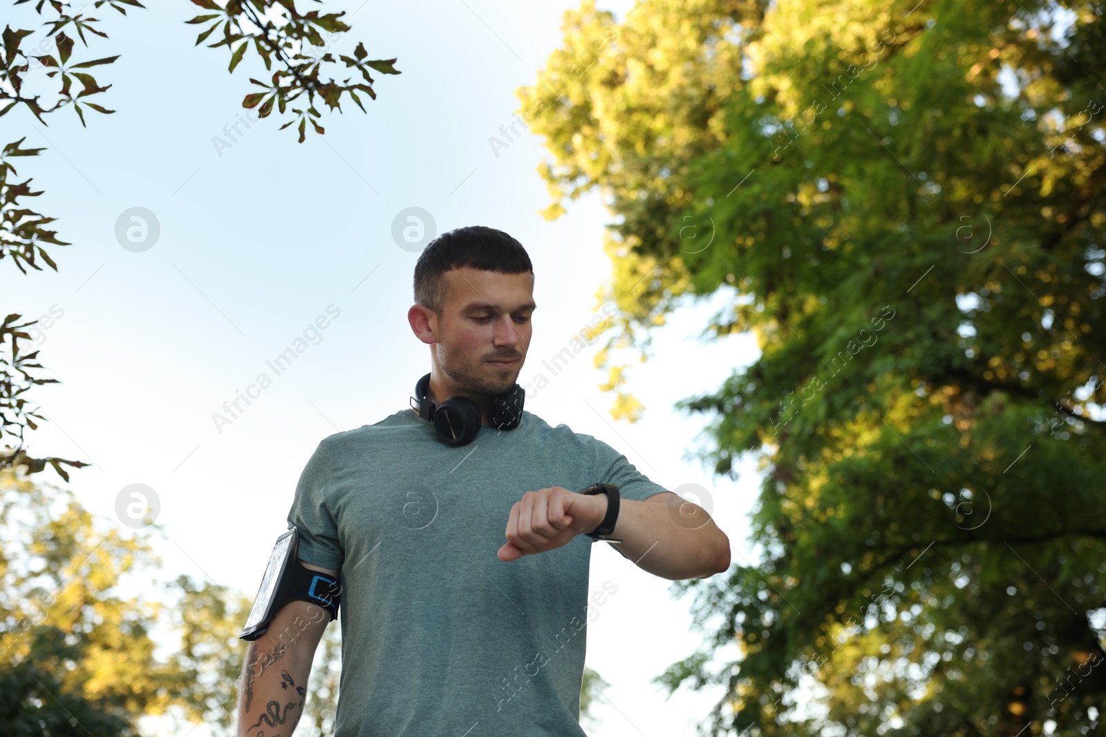 Athletic young man in sportswear checking fitness tracker before running outdoors, low angle view. Space for text Photo of Athletic young man in sportswear checking fitness tracker before running outdoors, low angle view. Space for text