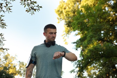 Photo of Athletic young man in sportswear checking fitness tracker before running outdoors, low angle view. Space for text